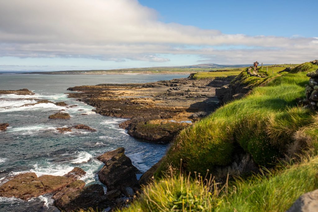 AKphoto (100) Coastal landscape with green cliffs and rocky shore along the Atlantic Ocean under a partly cloudy sky in Ireland.