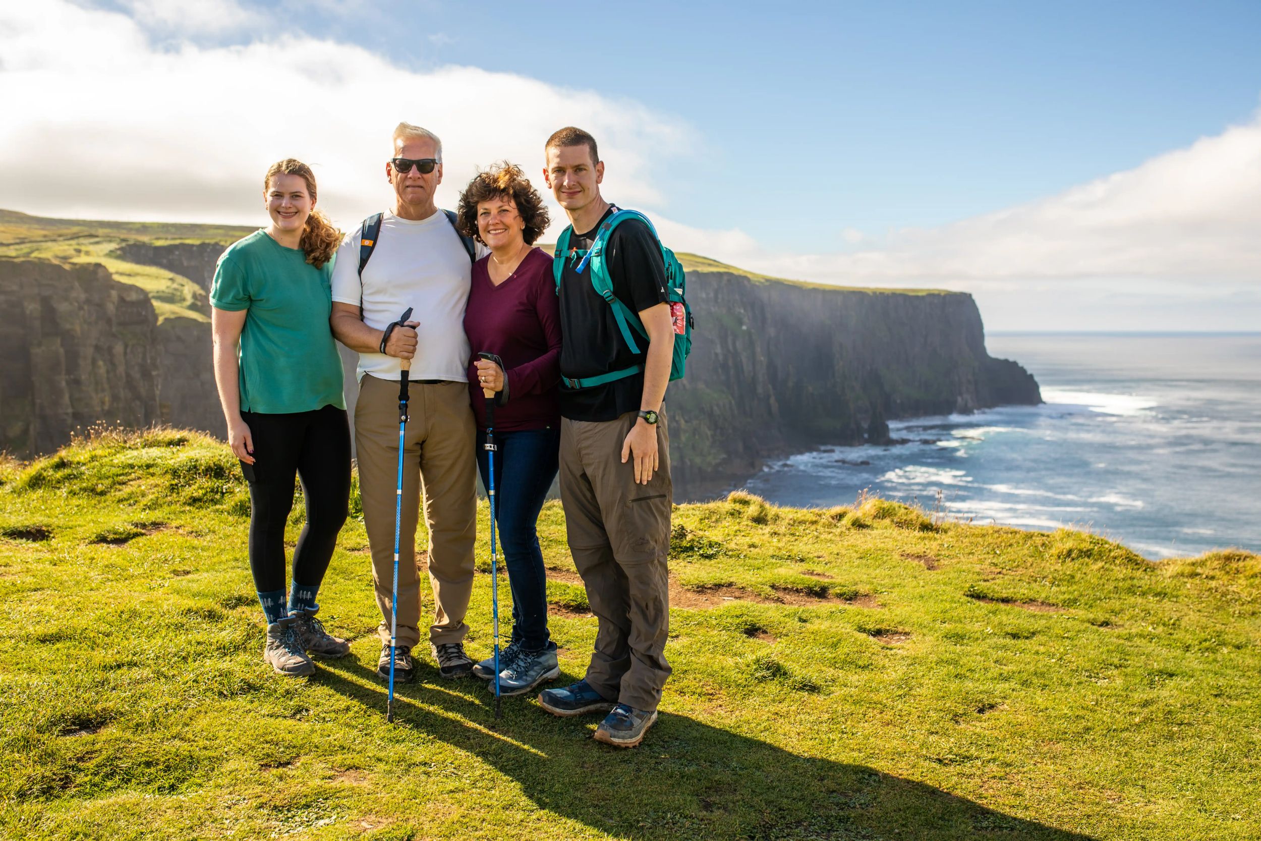 A group of hikers pose on cliffs by the sea under a bright sky in Ireland, enjoying a scenic outdoor adventure.