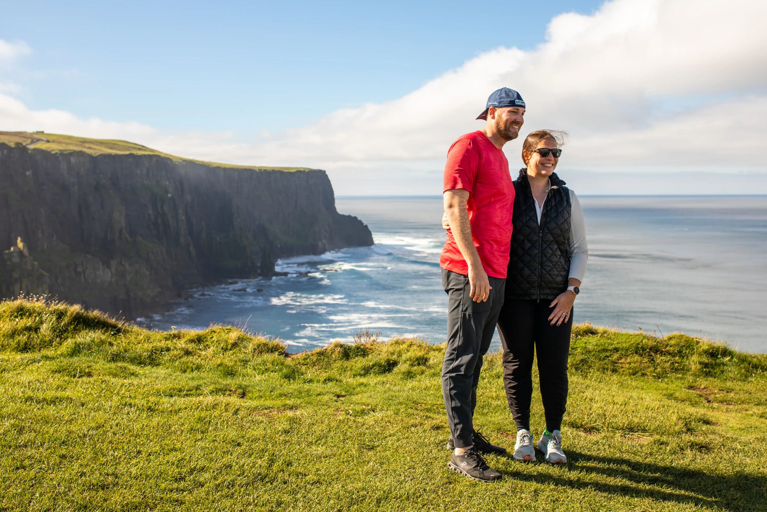 Couple enjoying scenic view of cliffs and ocean in Ireland on a sunny day.