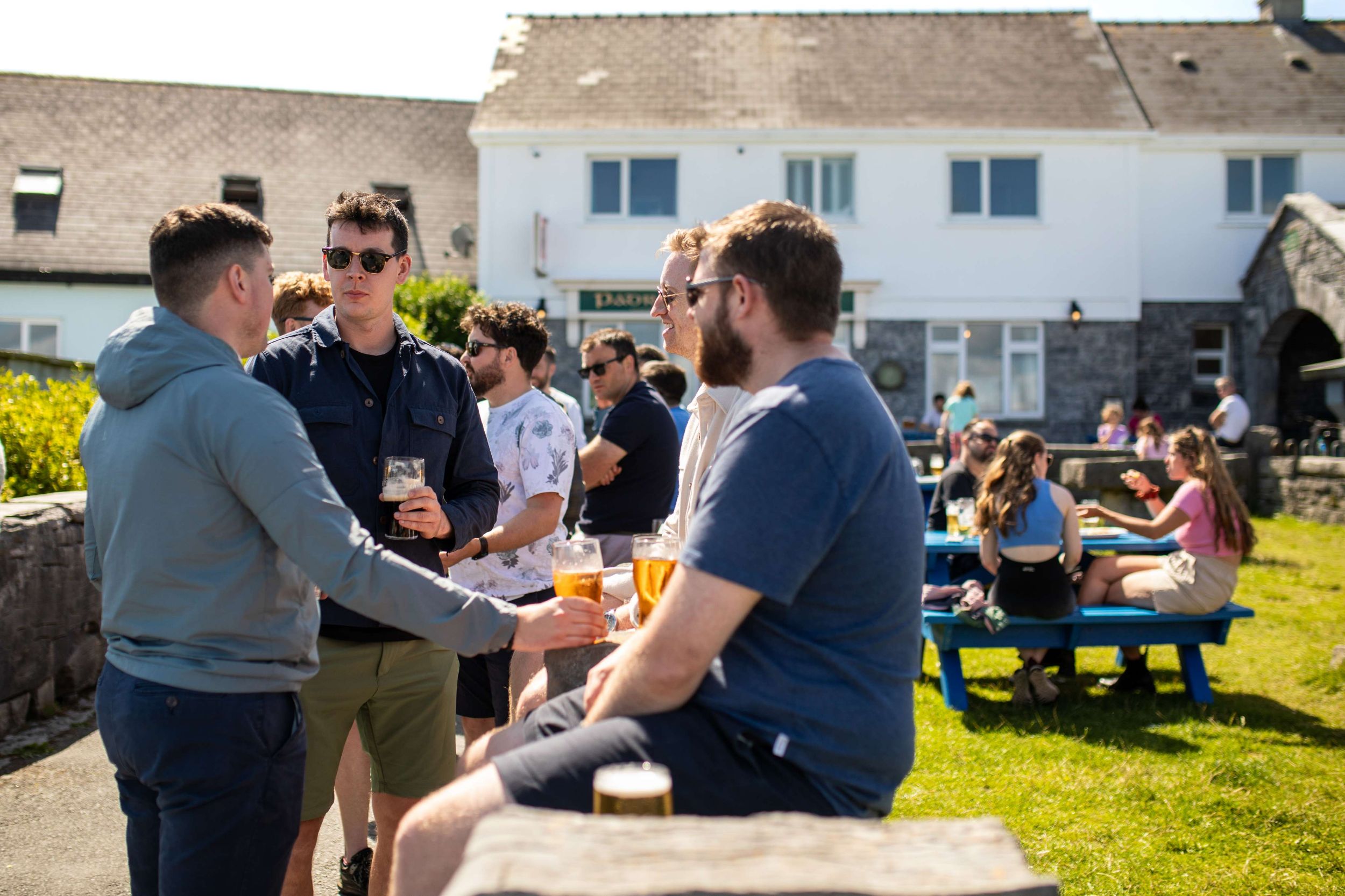 Group of friends enjoying drinks outdoors at a sunny British pub garden.