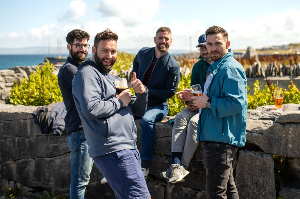 AKphoto (163) Group of friends enjoying drinks by the sea, scenic coastal backdrop, sunny day, cheering and relaxed atmosphere.