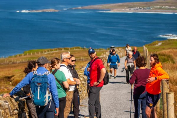 Group of hikers on a scenic coastal path with ocean views on a sunny day.