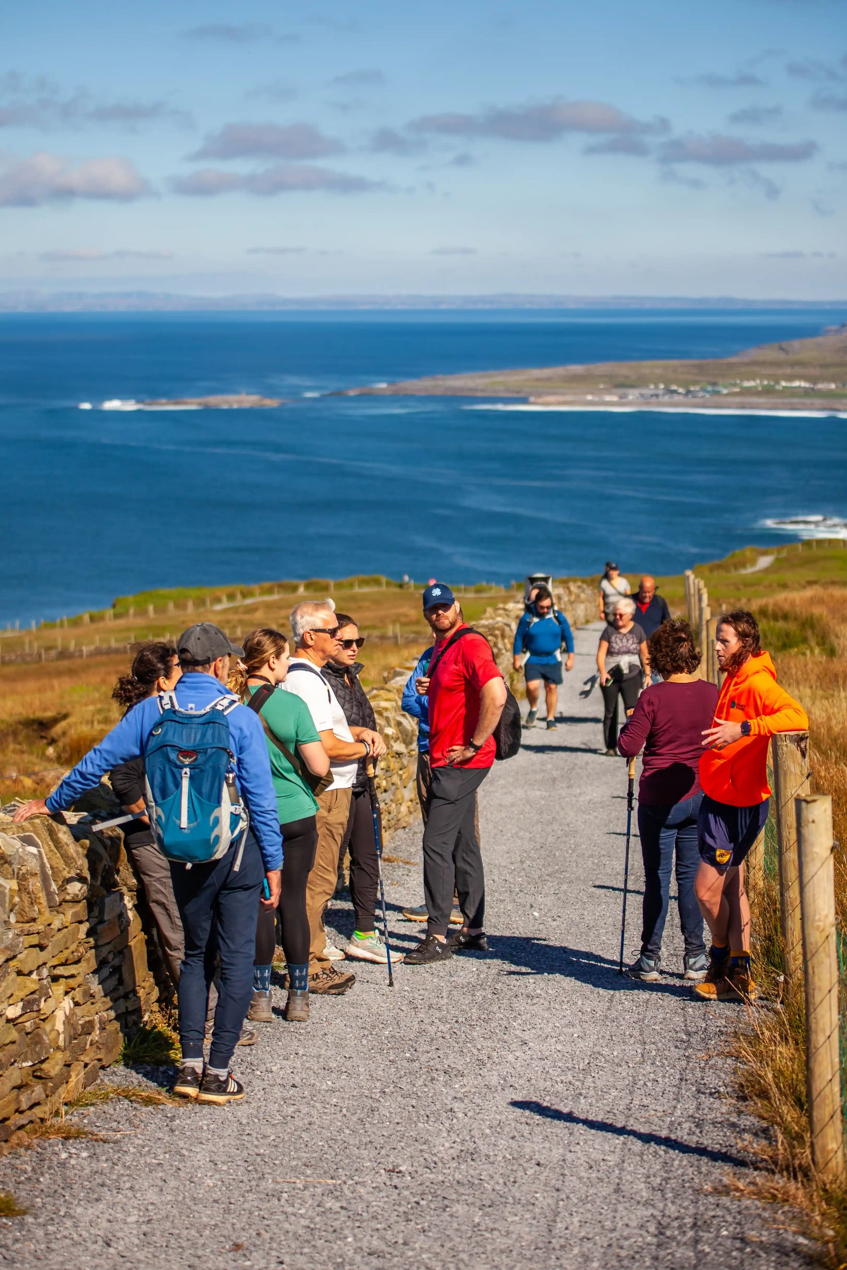 Group of hikers on a scenic coastal path with ocean views on a sunny day.