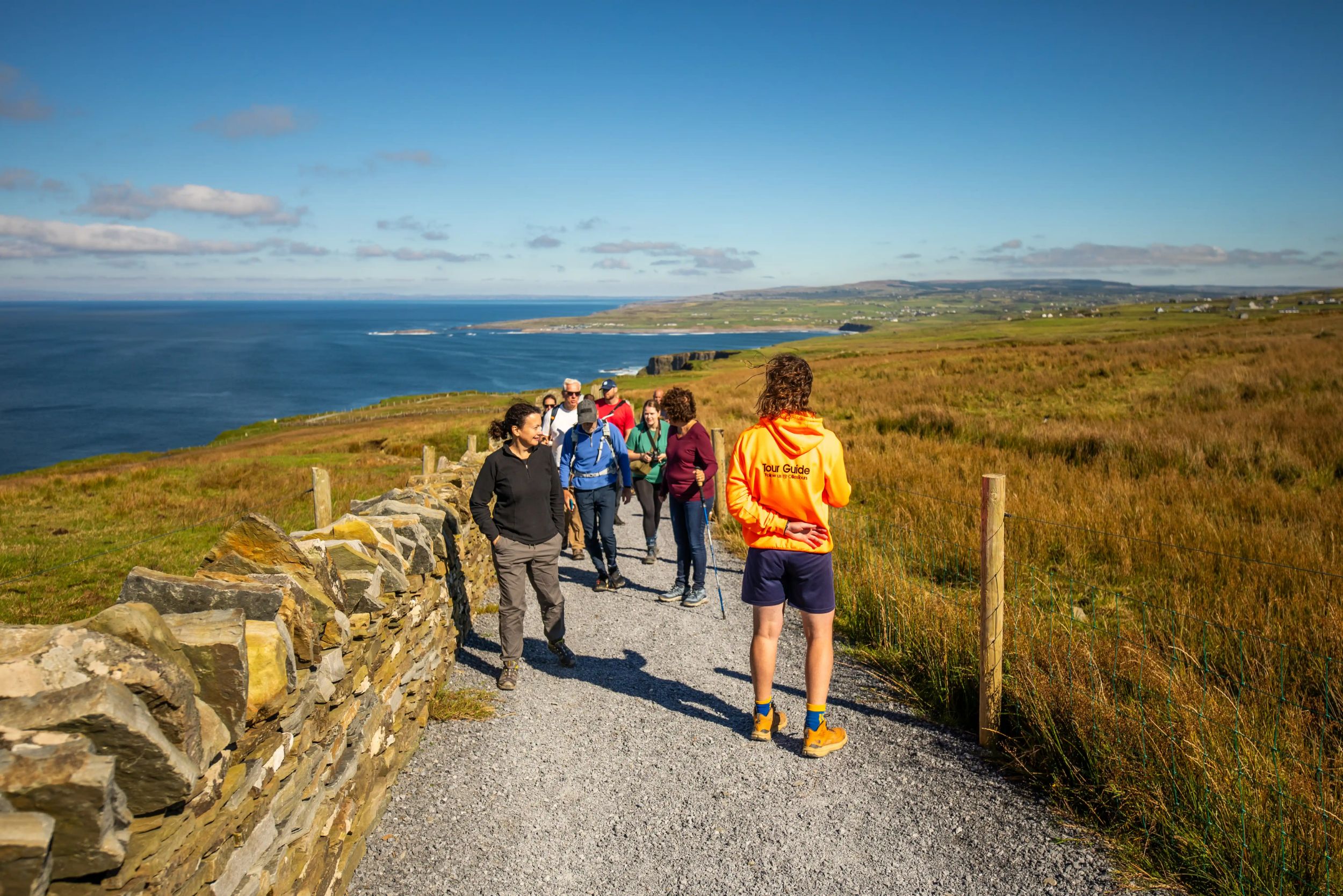 Tour group exploring scenic coastal trail under clear blue sky.