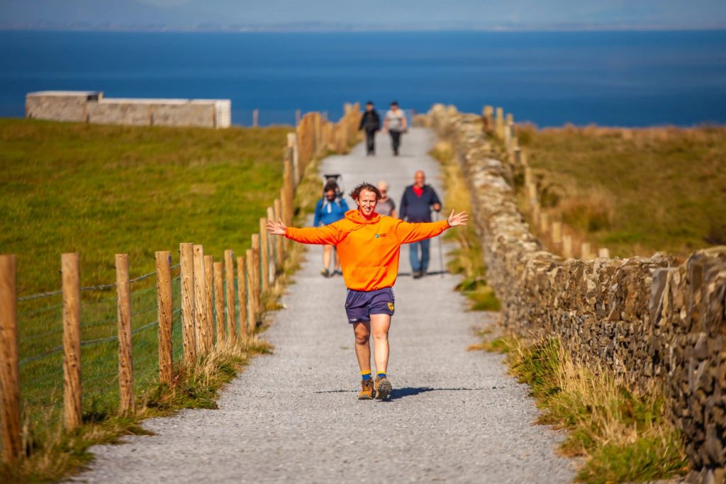 Ollie running joyfully on a coastal path with scenic ocean view in the background.