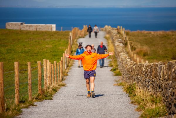 Ollie running joyfully on a coastal path with scenic ocean view in the background.