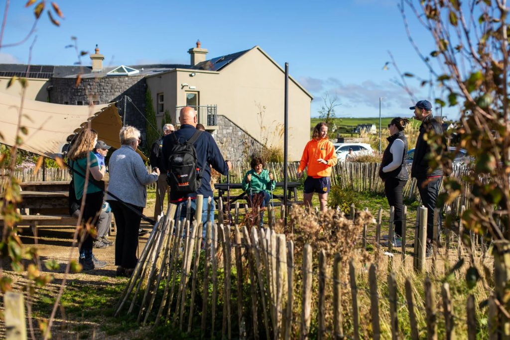 AKphoto (2) Group gathered outdoors near a house, engaging in a discussion on a sunny day.