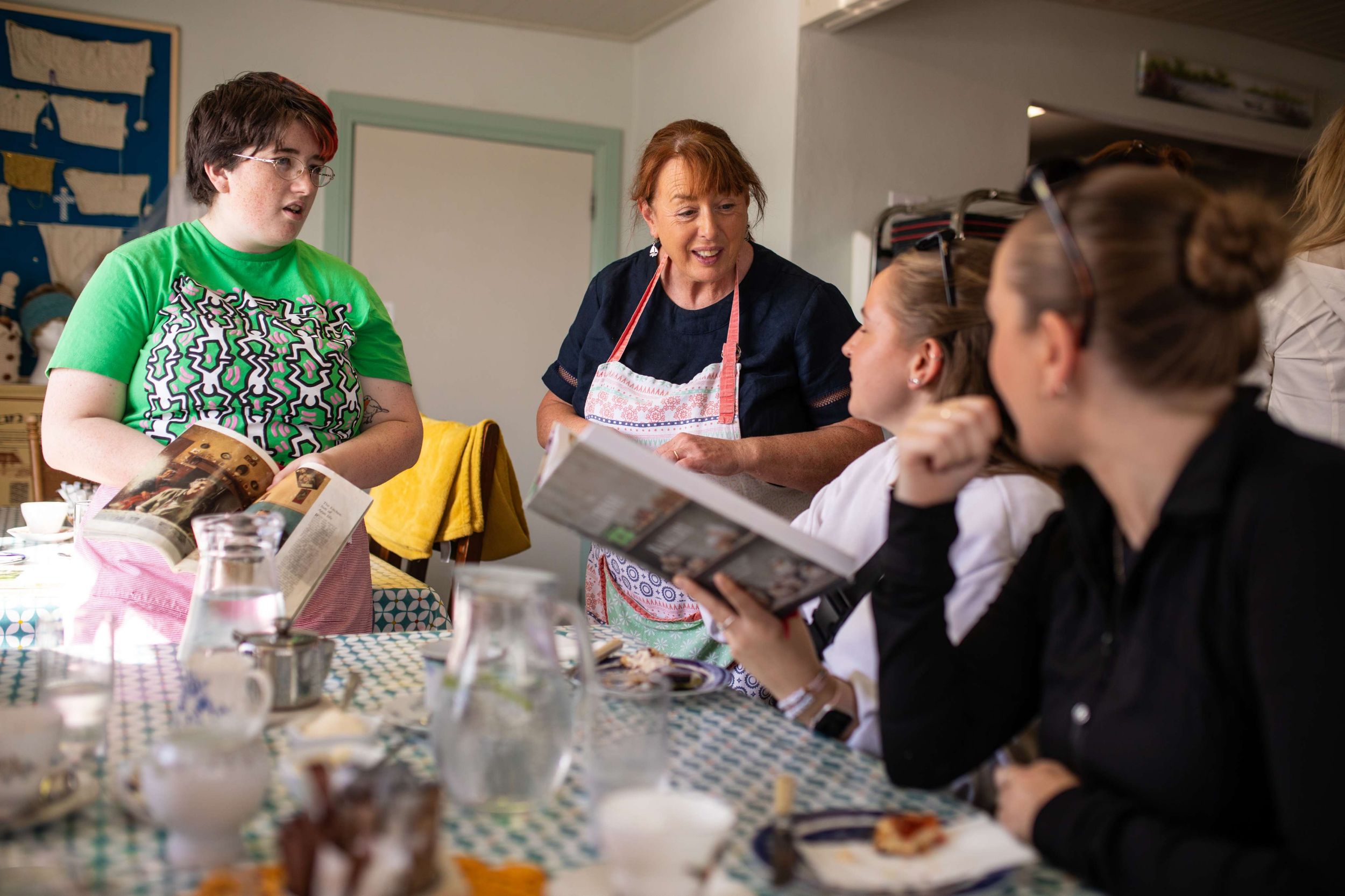 Group discussion in a cosy kitchen with books and tea, focusing on recipes and cooking tips.