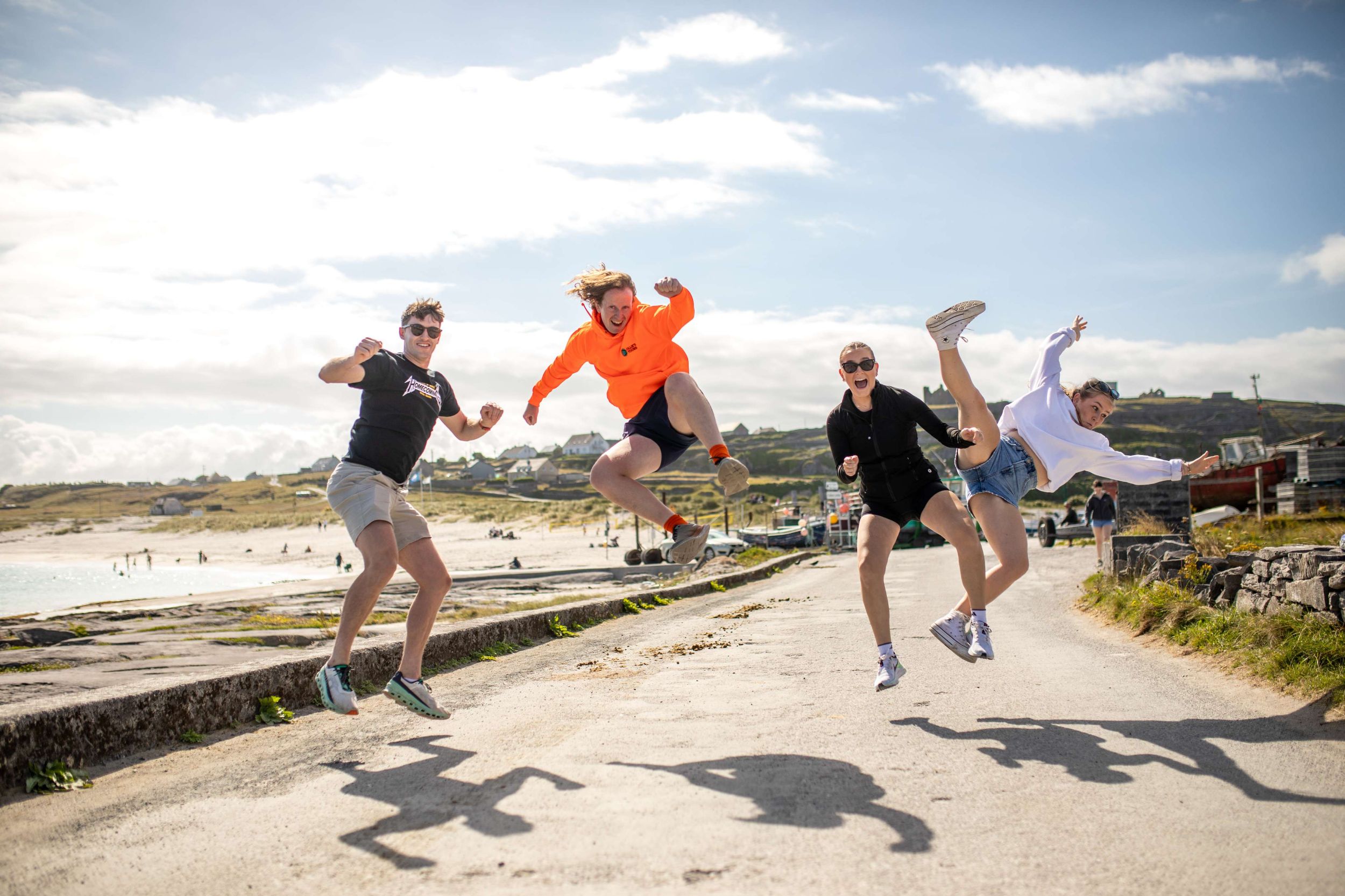 Group of friends joyfully jumping by a sunny beach in Ireland, showcasing fun and outdoor adventure.