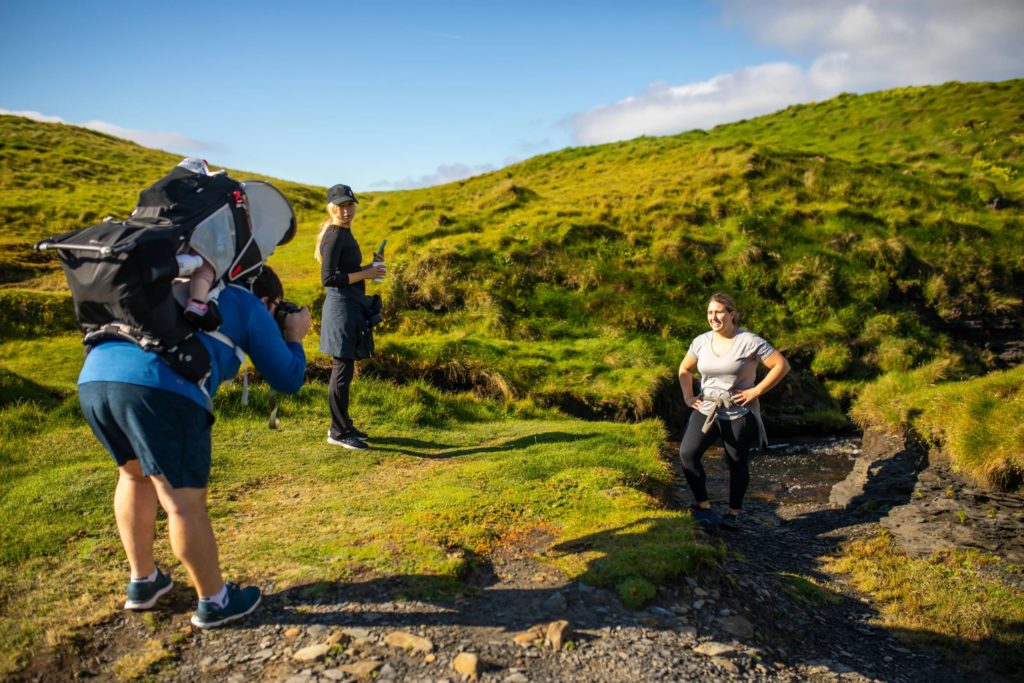 AKphoto (30) Family hiking adventure on a sunny day, capturing photos in a scenic green landscape.