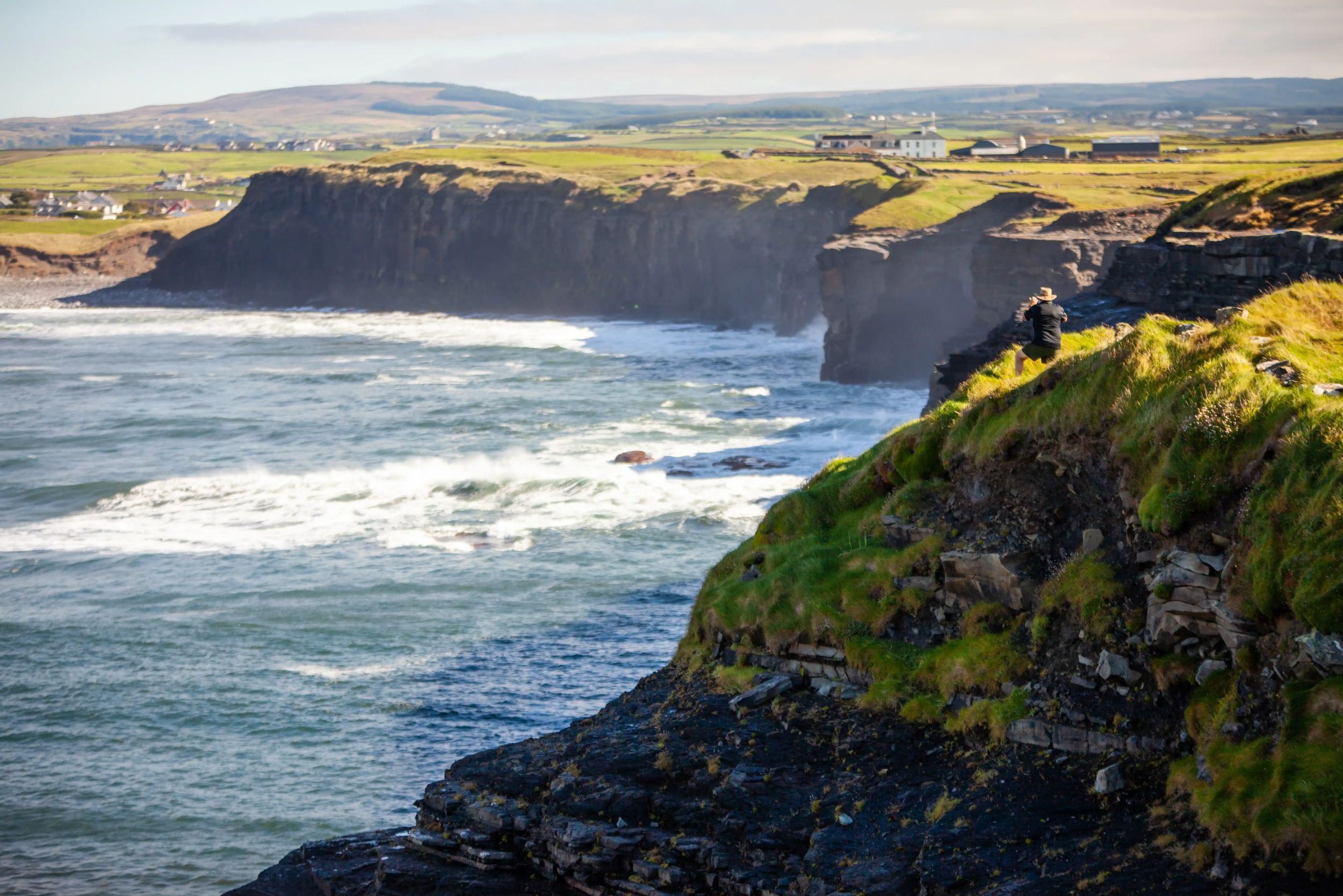 Stunning view of rugged cliffs with waves crashing, capturing the wild beauty of the Irish coastline under a clear sky.