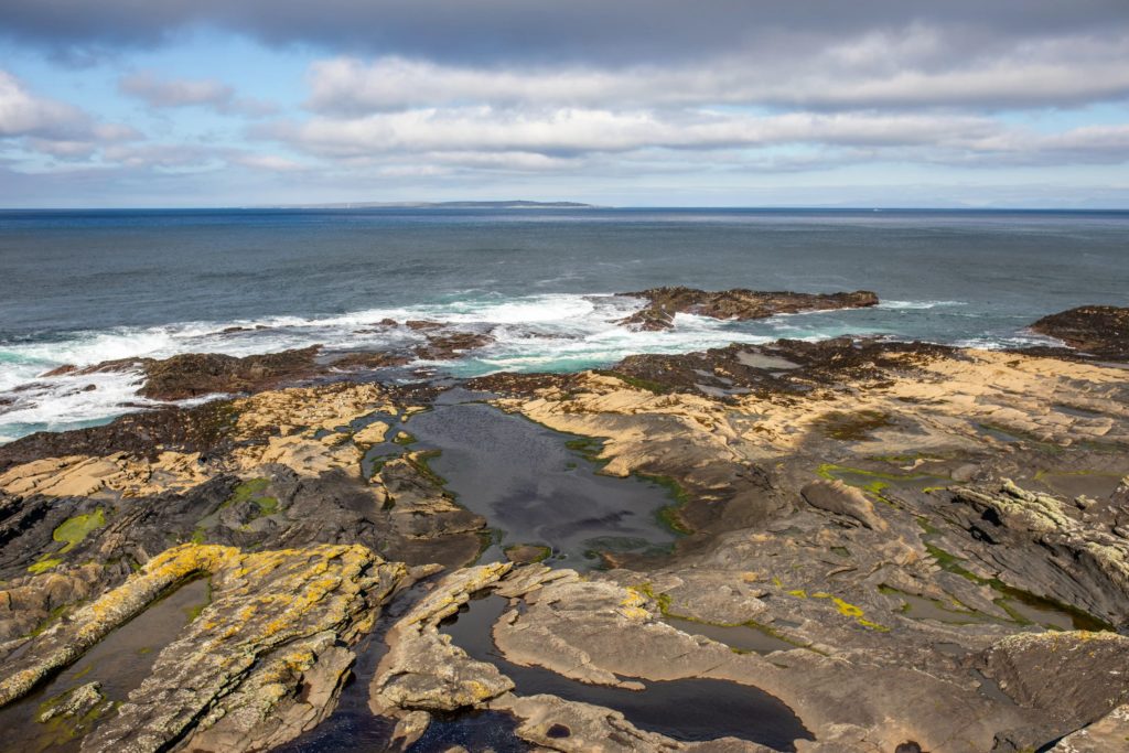 AKphoto (93) Rocky coastal landscape with tide pools and waves under a cloudy sky, showcasing natural beauty and rugged terrain.